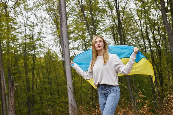 Supportive independent blonde woman standing in the forest with the Ukrainian flag waving it — Stock Photo