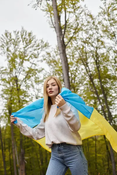 Patriótica mujer rubia aventurera orgullosamente sosteniendo bandera nacional ucraniana en el bosque, la libertad - foto de stock