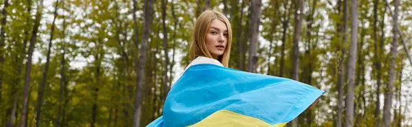 Back view of female young blonde hiker, holding the Ukrainian flag and turning to camera, banner — Stock Photo