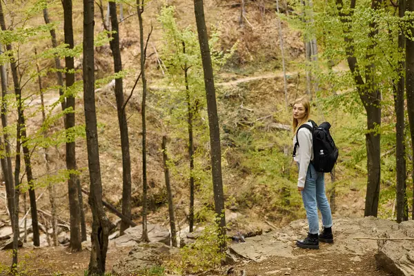 Side view of blonde young woman adventurer standing on forest trail, discovering new paths — Stock Photo