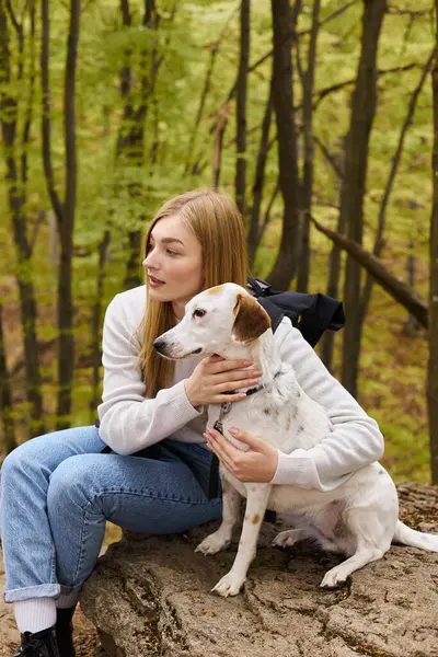 Caring blonde woman hugging her dog, while having a halt on forest trip, both looking away — Stock Photo