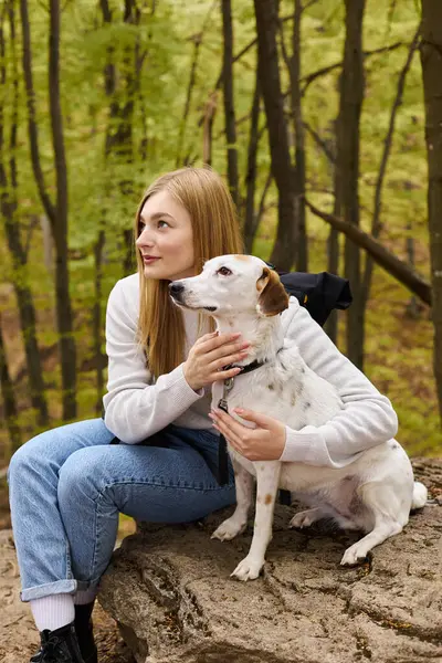 Sorrindo mulher loira abraçando seu cão, enquanto tendo uma parada na viagem pela floresta, ambos olhando para longe — Fotografia de Stock