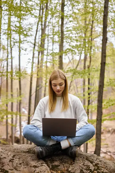 Blonde, entspannte Frau im Wald, sitzt auf Felsbrocken mit Laptop in Lotusposition — Stockfoto