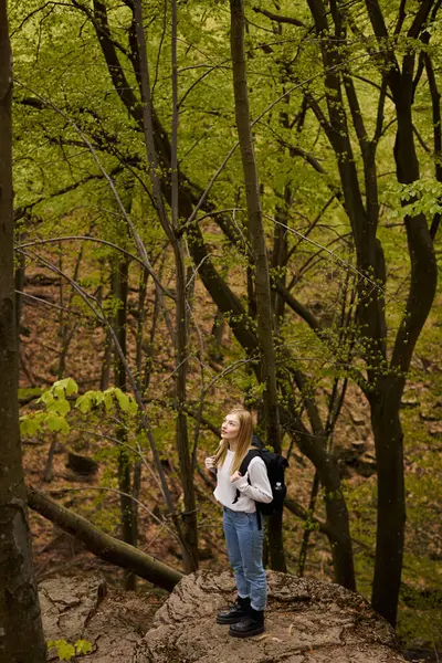 Mujer rubia excursionista con mochila caminando a través de un bosque para mochilero aventura en la naturaleza - foto de stock