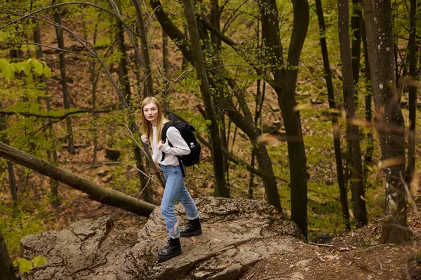 Rubia tranquila mujer bonita excursionista con mochila caminando a través de un bosque mirando a la cámara - foto de stock