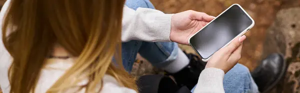 Cropped image of woman holding phone in hands sitting in forest scenery and texting, banner — Stock Photo