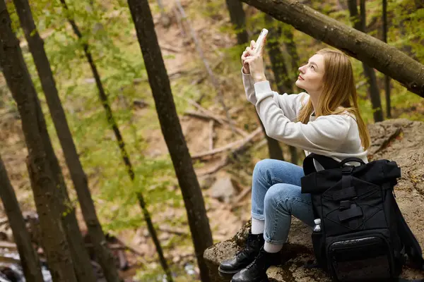 Vista lateral da jovem loira viajante tirando fotos de paisagens na floresta enquanto caminha — Fotografia de Stock