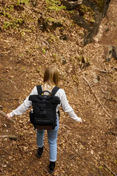 Back view of active blonde female hiker wearing sweater and jeans crossing the forest while hiking — Stock Photo