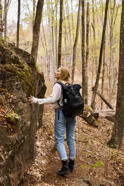 Vista posteriore della curiosa donna bionda che indossa lo zaino in escursione e cammina vicino a scogliera rocciosa — Foto stock
