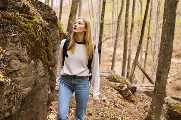 Avventurosa donna bionda che indossa lo zaino in viaggio a piedi e camminando vicino a scogliera rocciosa — Foto stock