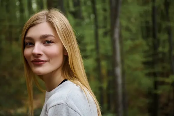 Lächelnd fröhlich schöne blonde Frau schaut in die Kamera, während sie im Wald spazieren geht — Stockfoto