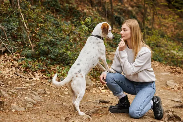 Cheerful woman training her pet dog while having backpacking trip with companion — Stock Photo