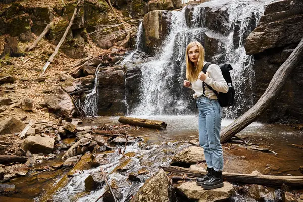 Активная блондинка-туристка, стоящая у лесного ручья и идущая по скалам возле водопада — стоковое фото