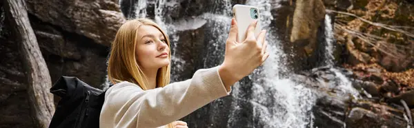 Jeune femme blonde prenant selfie près de la cascade de montagne dans la forêt pendant la randonnée, bannière — Photo de stock