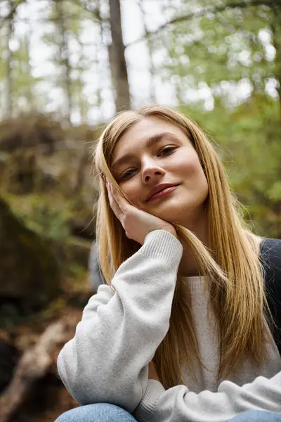 Portrait of dreamy woman touching cheek and smiling at camera in forest while hiking — Stock Photo