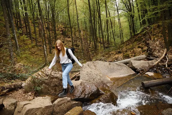 Mujer con mochila de senderismo y caminar sobre la roca del río de montaña en el bosque. Turista femenina solitaria - foto de stock