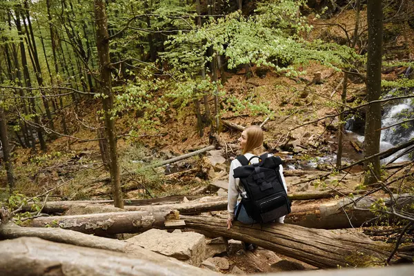 Rückenansicht einer jungen blonden Wanderin mit schwarzem Rucksack, die beim Trekking sitzt und ausruht — Stockfoto