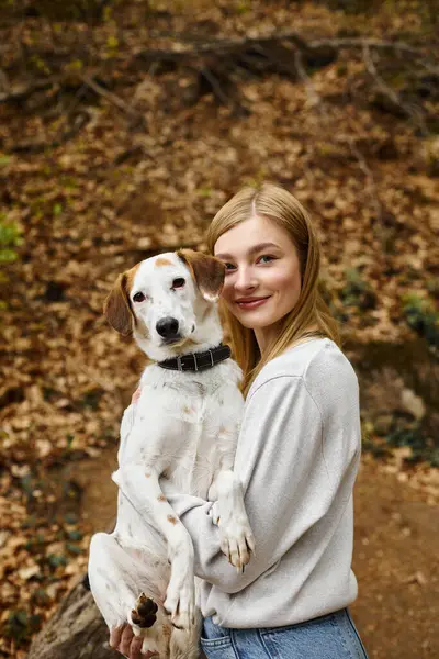 Junge Frau hält ihren Hund in den Händen und umarmt sich bei Wanderrast mit Berg- und Waldblick — Stockfoto