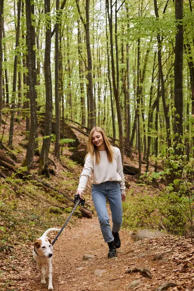 Laughing joyful blonde hiker girl walking dog in woods in forest while trekking, adventure — Stock Photo