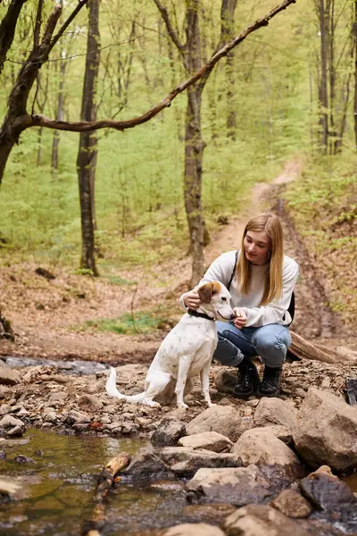 Smiling woman hugging gently her dog companion and looking at pet while walking in forest — Stock Photo