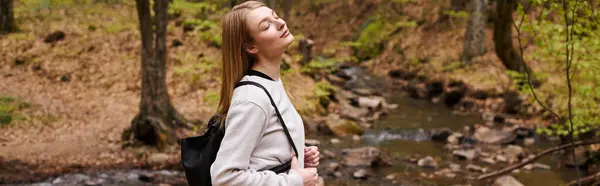 Young blonde female standing with eyes closed in woods. Portrait of relaxed girl in forest, banner — Stock Photo