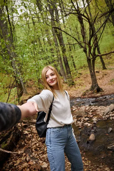 Porträt einer lächelnden jungen Frau, die die Hand ihres Freundes hält, während sie im Wald spaziert — Stockfoto