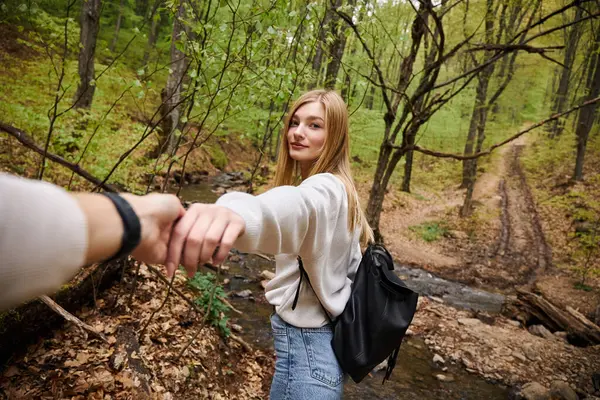 Mujer joven liderando camino, punto de vista foto de pareja cogida de la mano cruzando el arroyo en el bosque - foto de stock