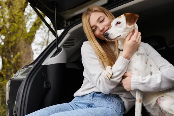 Chica feliz interactuando con su mascota mirando al perro en el descanso de senderismo se detiene en la parte trasera del coche - foto de stock