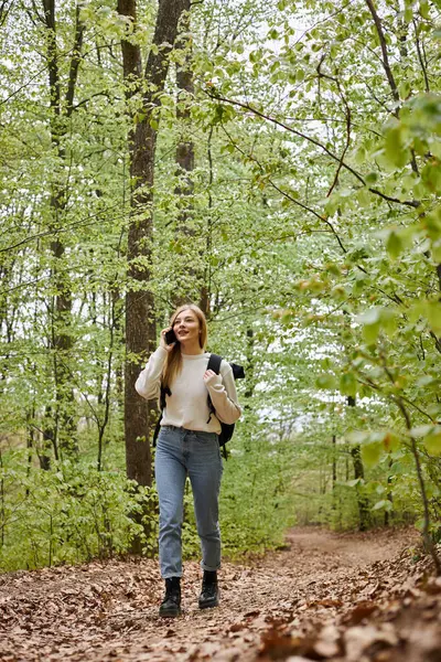 Mujer rubia bonita viajero con mochila hablando por teléfono caminando en el paisaje del bosque - foto de stock