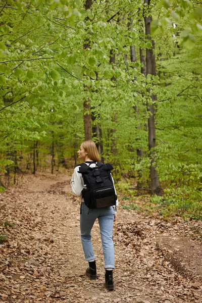 Voltar ver foto de mulher loira viajante com mochila à procura de direção andando no caminho da floresta — Fotografia de Stock