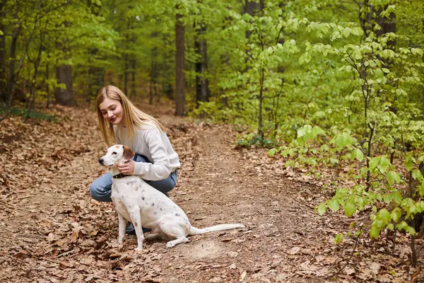 Chica senderista sonriente interactuando con su mascota mirando hacia la dirección mientras camina descanso con vista al bosque - foto de stock