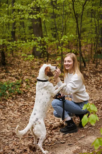 Sorrindo menina caminhante interagindo com seu treinamento animal de estimação enquanto caminhadas resto com vista para a floresta — Fotografia de Stock