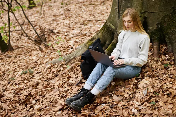 Young calm woman hiker with laptop on her knees working remote while sitting in forest on trip — Stock Photo
