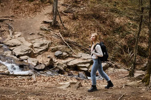 Jovem caminhante atravessando o riacho da floresta, tendo viagem mochila perto na floresta — Fotografia de Stock