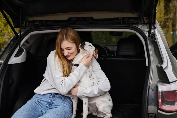 Imagem de mulher gentilmente abraçando seu cão branco sentado na parte de trás do carro. Companheiro de cão — Fotografia de Stock