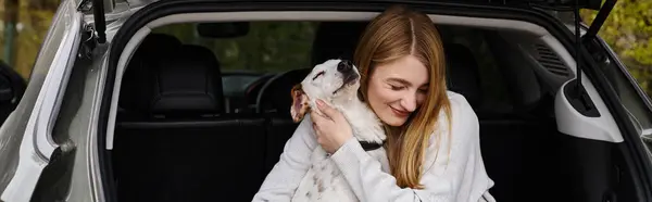 Image of woman gently hugging her white dog sitting at back of car, dog companion banner — Stock Photo
