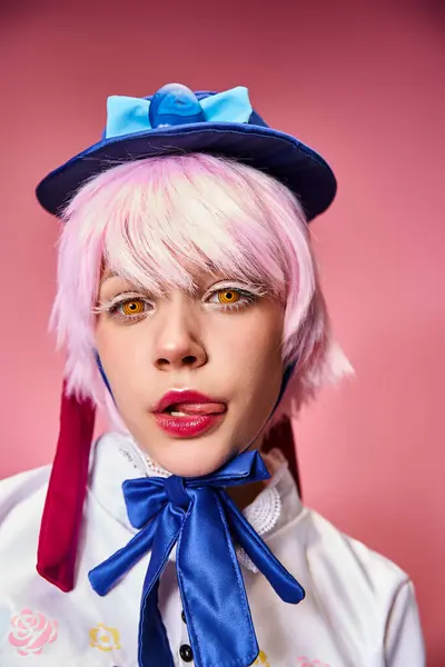 Verführerische junge Cosplayerin streckt ihre Zunge heraus und blickt vor rosa Hintergrund in die Kamera — Stockfoto