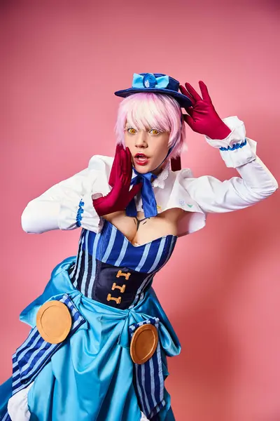 Atractivo cosplayer femenino sexy en sombrero azul y traje vibrante mirando a la cámara en el telón de fondo rosa - foto de stock