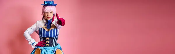 Шикарний жіночий косплеєр у яскравій сукні з синім капелюхом, що вказує на камеру на рожевому тлі, банер — стокове фото