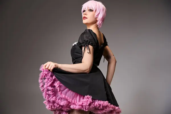 Atractiva mujer cosplaying sexy personaje de anime con pelo rosa y mirando hacia otro lado sobre fondo gris - foto de stock