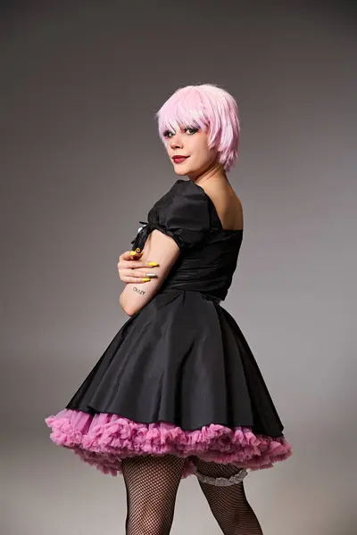 Sexy mujer con estilo en vestido negro con el pelo rosa cosplaying personaje de anime y mirando a la cámara - foto de stock