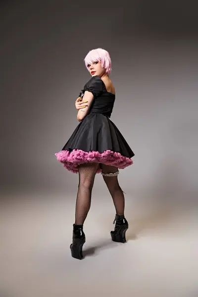 Sexy mujer con estilo en vestido negro con el pelo rosa cosplaying personaje de anime y mirando a la cámara - foto de stock