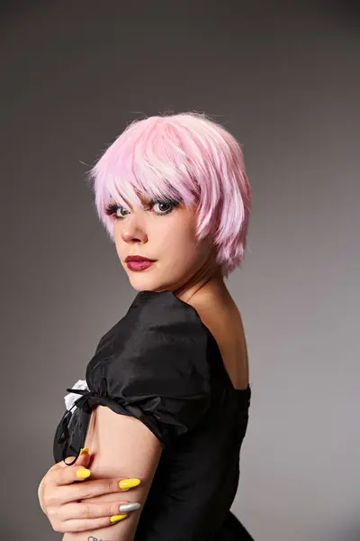 Seductora mujer elegante en vestido negro con el pelo rosa personaje de anime cosplaying y mirando a la cámara - foto de stock