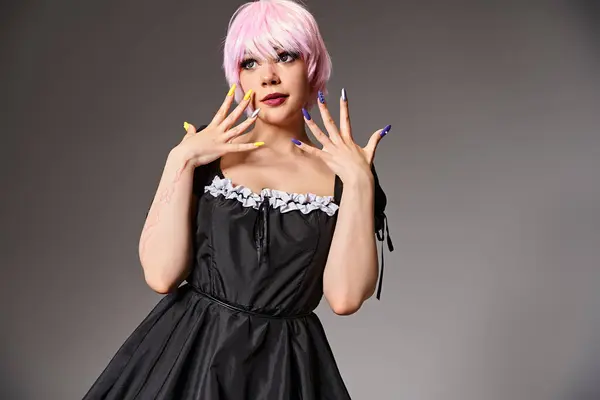 Сексуальная женщина косплеер в черном платье с розовыми волосами позирует на сером фоне и смотрит в сторону — стоковое фото