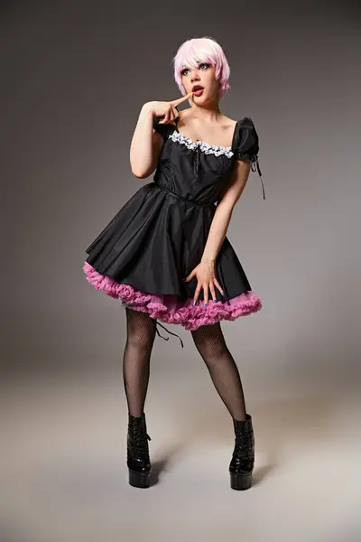 Sexy cosplayer femenino en vestido negro con pelo rosa posando sobre fondo gris y mirando hacia otro lado - foto de stock
