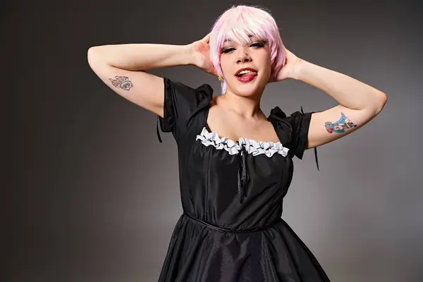 Alegre cosplayer femenino en traje de criada sexy con el pelo rosa pegando su lengua y mirando a la cámara - foto de stock