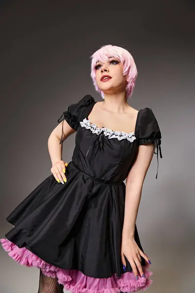 Hermoso cosplayer de pelo rosa en traje de criada sexy posando sobre fondo gris y mirando hacia otro lado - foto de stock