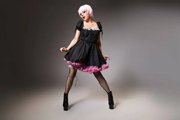 Hermoso cosplayer de pelo rosa en traje de criada sexy posando sobre fondo gris y mirando hacia otro lado - foto de stock