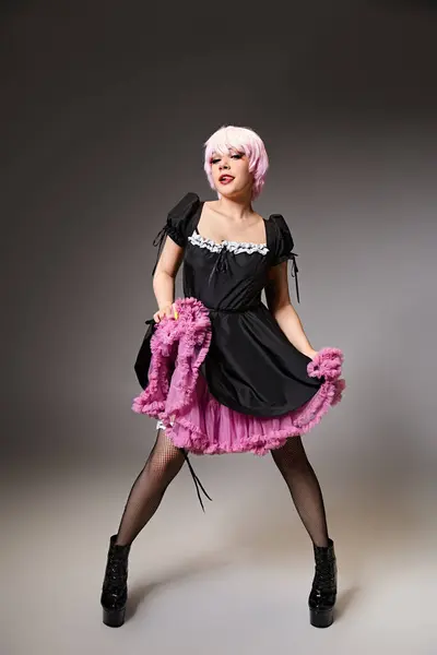 Веселая женщина-косплеер в костюме сексуальной горничной с розовыми волосами, засовывающими язык и смотрящей в камеру — стоковое фото