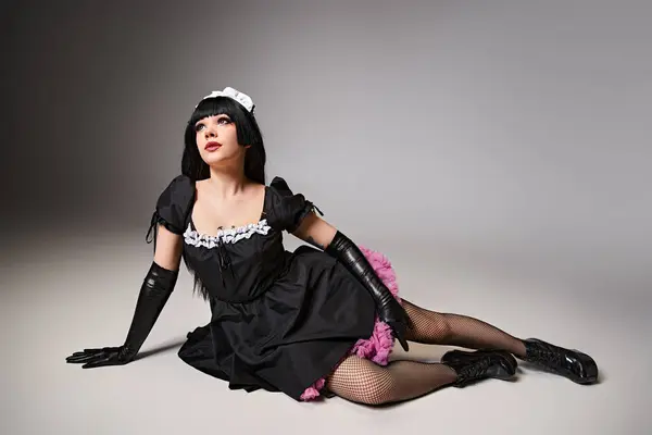 Attraente cosplayer sexy in costume da cameriera nera posa attivamente e guardando lontano su sfondo grigio — Foto stock